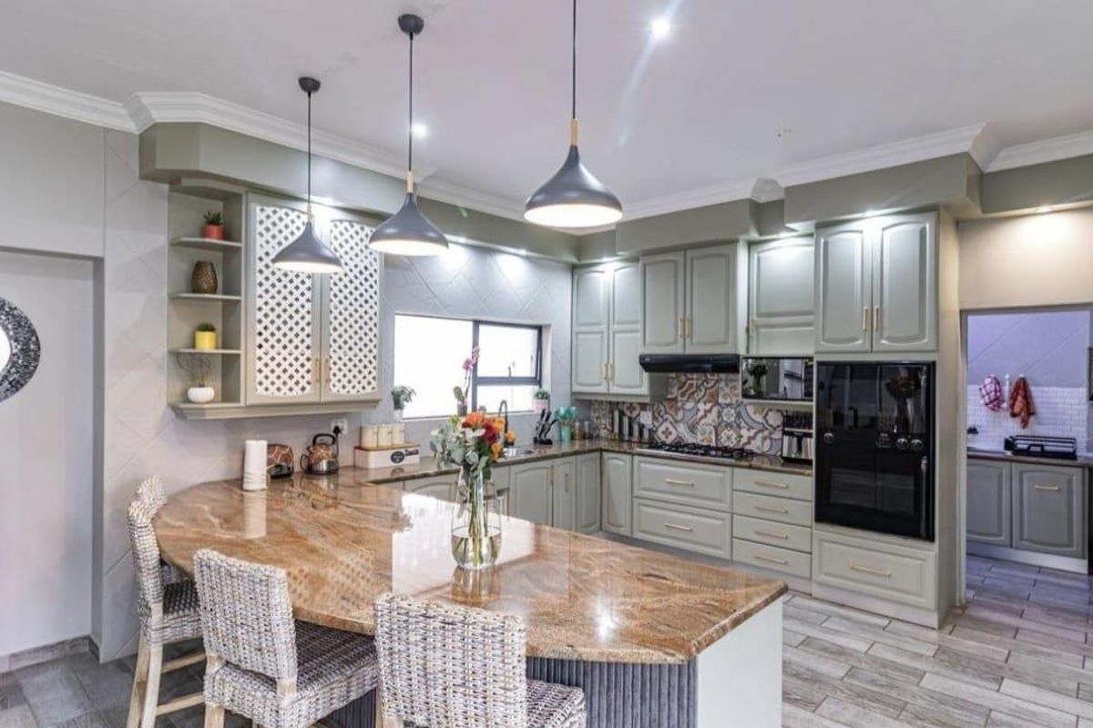 Modern kitchen featuring sage green cabinetry, granite countertops, integrated appliances, and a breakfast bar, with an adjacent scullery area.