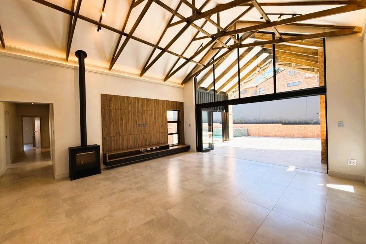 Spacious living area featuring high vaulted ceilings with exposed timber trusses, a modern fireplace, built-in media unit, and seamless access to the outdoor patio.