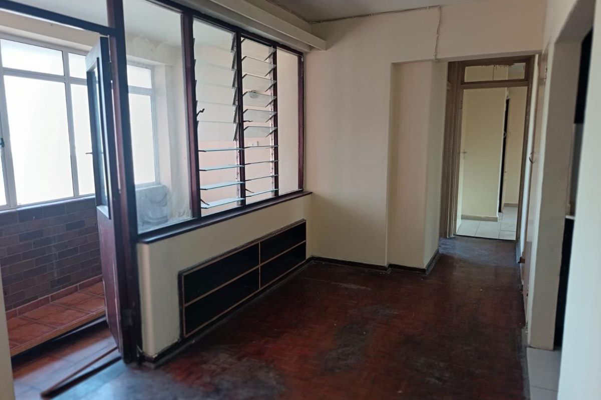 An empty living area featuring dark flooring, built-in shelving, and access to an enclosed balcony through a glass partition.