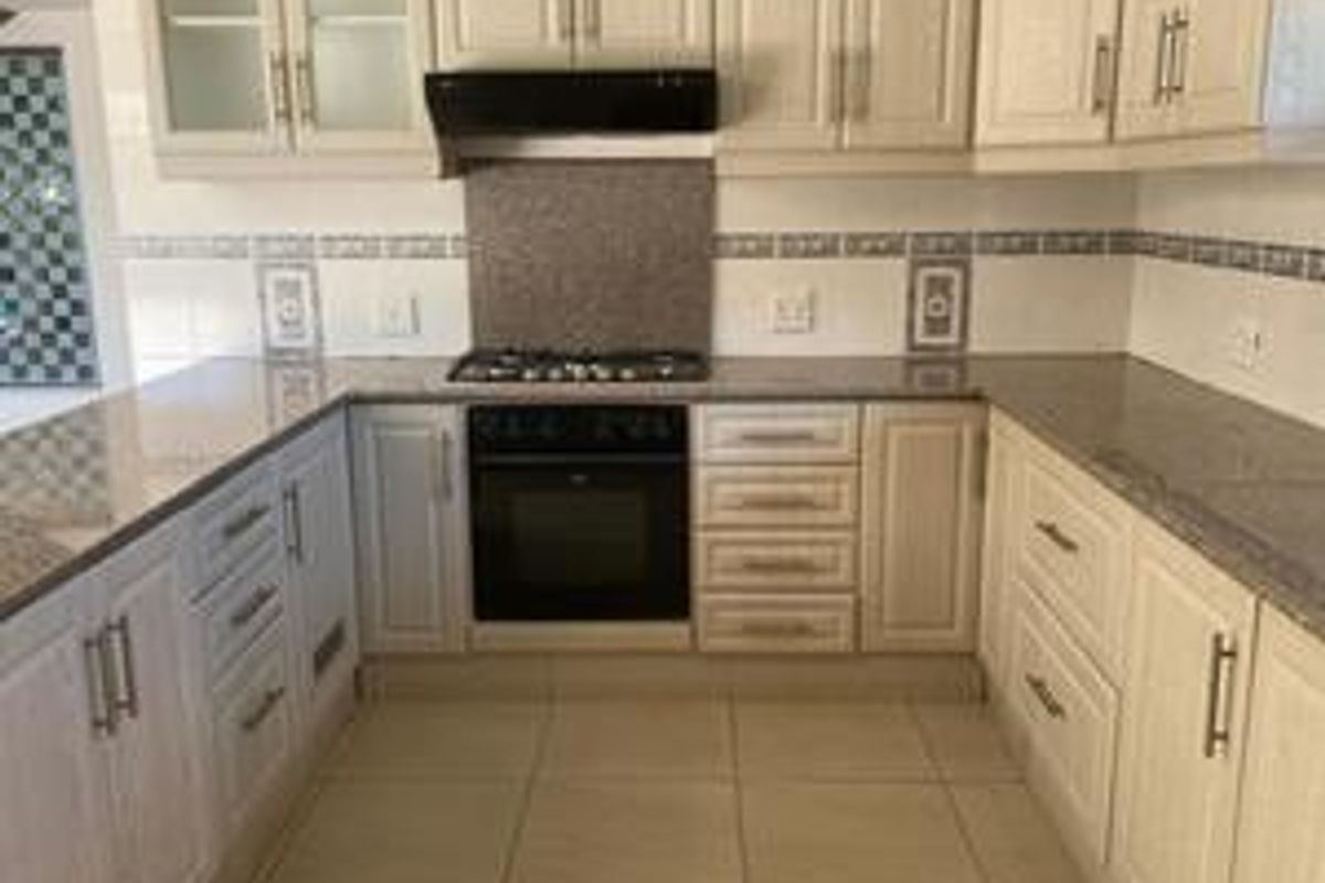 A clean, functional kitchen featuring light-toned cabinetry, granite countertops, a built-in oven, and a gas hob with an integrated extractor fan.