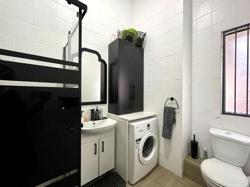 A functional bathroom featuring a vanity unit, shower enclosure, toilet, and integrated laundry space with built-in cabinetry and tiled finishes.