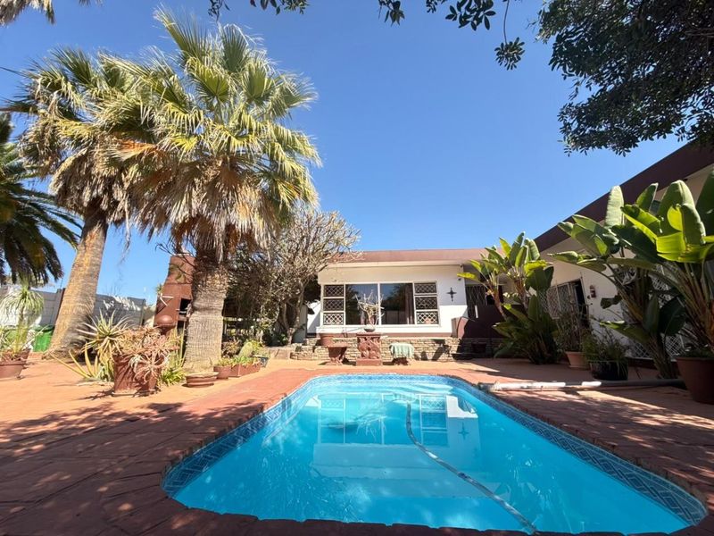 Outdoor pool area featuring a swimming pool set within a brick-paved courtyard, surrounded by established palm trees and garden landscaping.