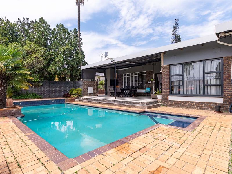 Outdoor entertainment area featuring a swimming pool, paved surround, and a covered patio attached to the main house structure.