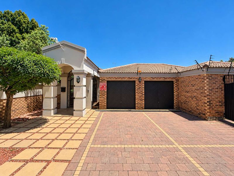 Front exterior view featuring a double garage, paved driveway, and a covered entrance with brick detailing and secure perimeter fencing.