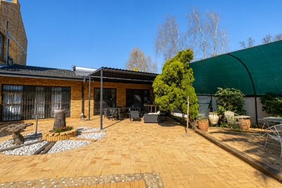 Spacious rear paved patio area featuring a covered section, brick exterior walls, and secure access points to the main dwelling.