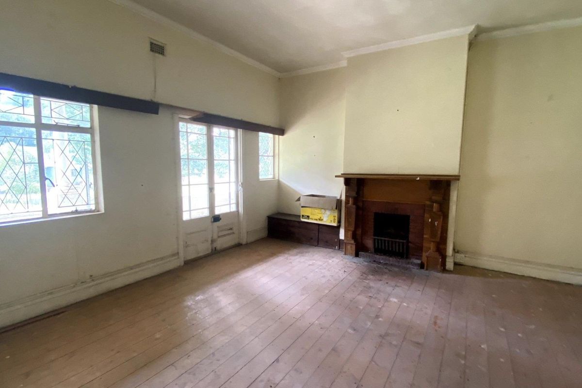 A spacious living room featuring original timber flooring, a traditional fireplace with a wooden mantel, and large windows providing natural light.