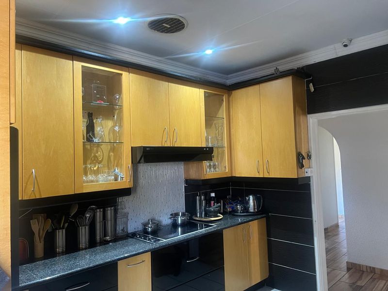 A functional kitchen featuring light wood cabinetry, black granite countertops, a built-in electric hob with extractor fan, and modern recessed lighting.