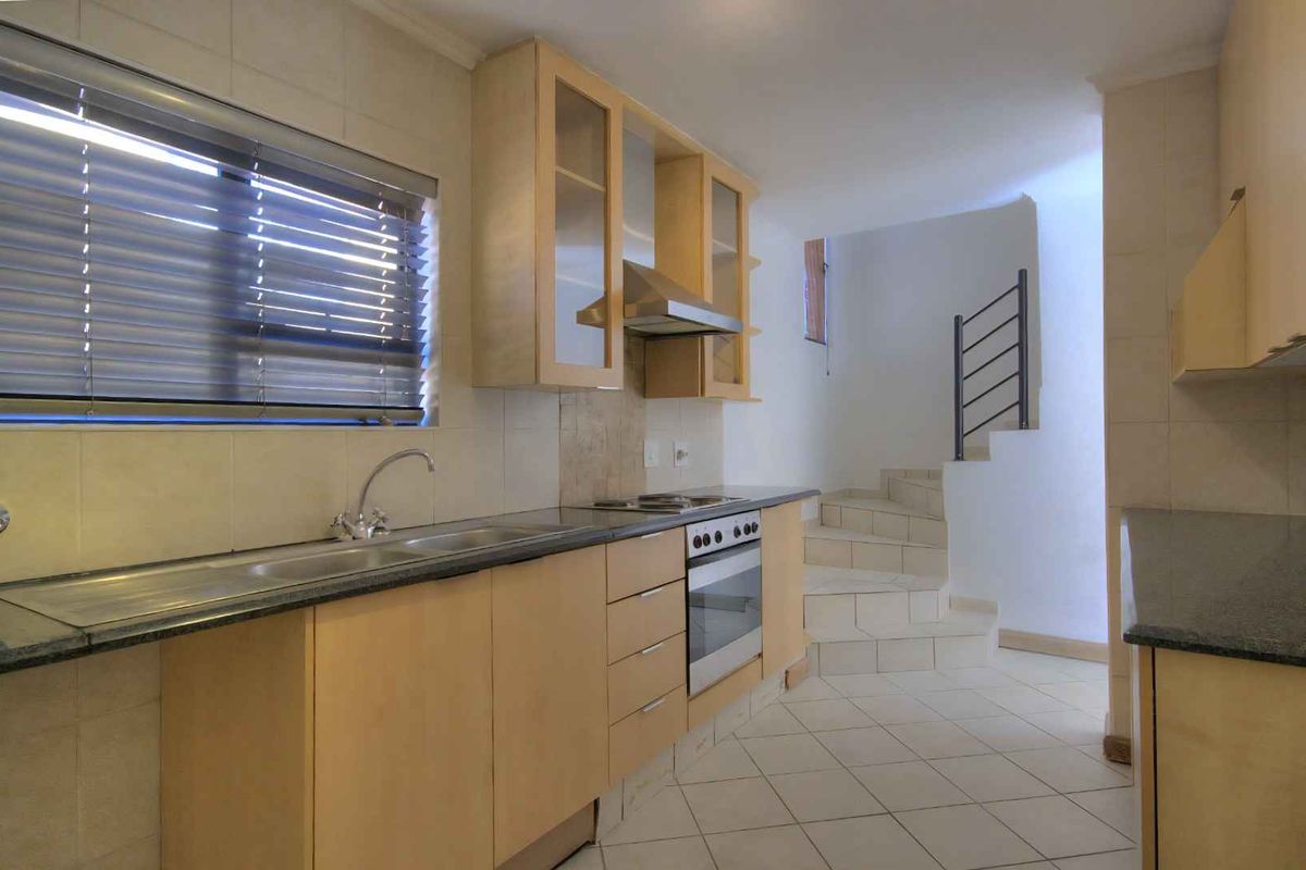 A functional kitchen featuring light wood cabinetry, granite countertops, built-in oven and hob, and tiled flooring, with an adjacent staircase.