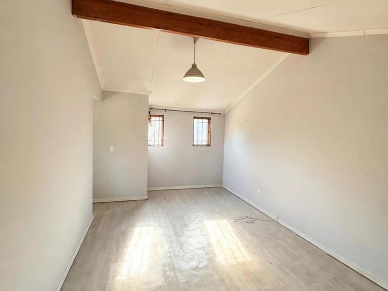 An empty living room featuring exposed timber ceiling beams, light-toned laminate flooring, and windows fitted with security bars.