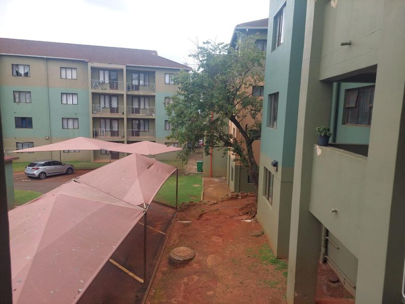 View of the apartment complex exterior featuring multi-story residential blocks, shade cloth carports, and communal outdoor areas.