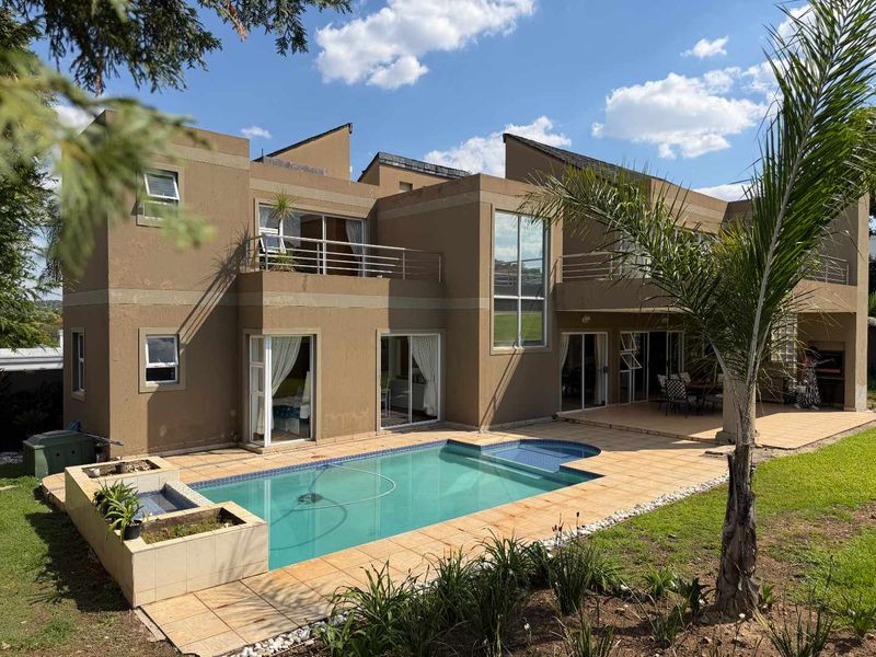 Rear view of a modern two-story house featuring a swimming pool, tiled patio area, upper-level balconies, and a built-in outdoor braai.