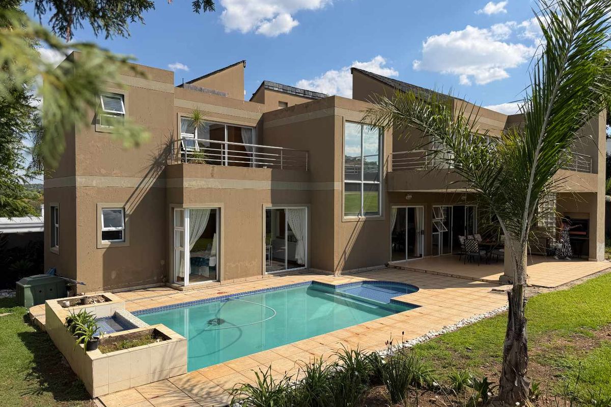 Rear view of a modern two-story house featuring a swimming pool, tiled patio area, upper-level balconies, and a built-in outdoor braai.
