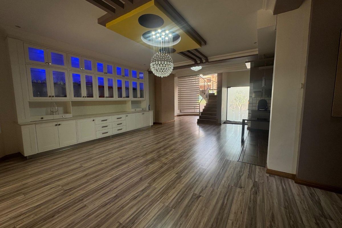 Spacious living area featuring extensive built-in cabinetry, modern laminate flooring, and a decorative recessed ceiling with a crystal chandelier.