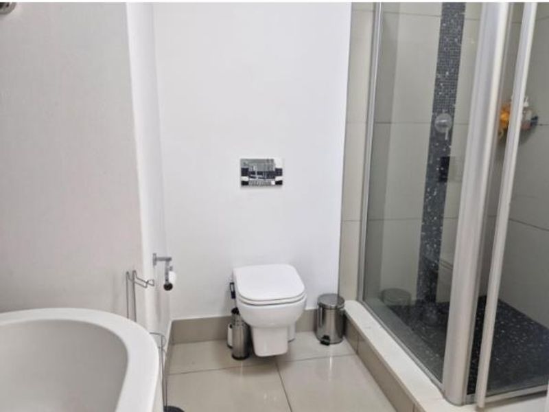 Modern bathroom featuring a wall-hung toilet with a concealed cistern and a glass-enclosed shower with decorative mosaic tile accents.