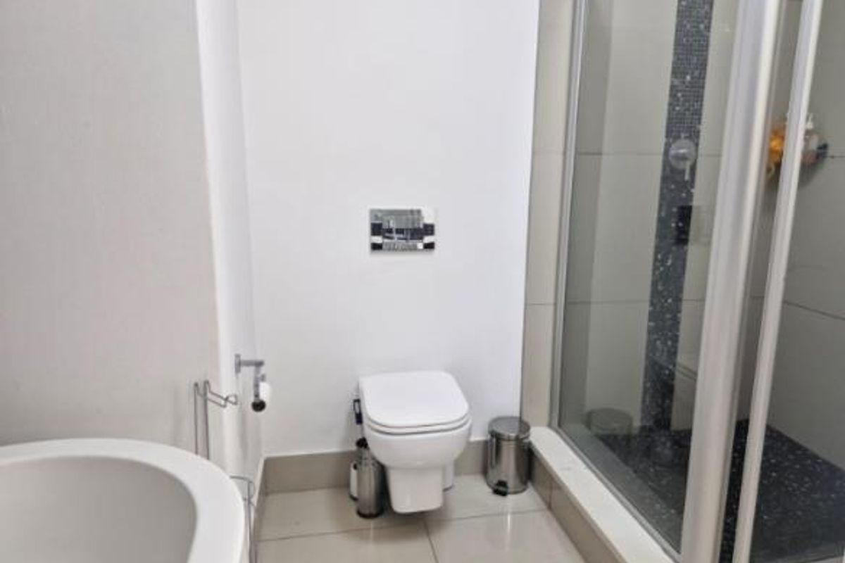 Modern bathroom featuring a wall-hung toilet with a concealed cistern and a glass-enclosed shower with decorative mosaic tile accents.