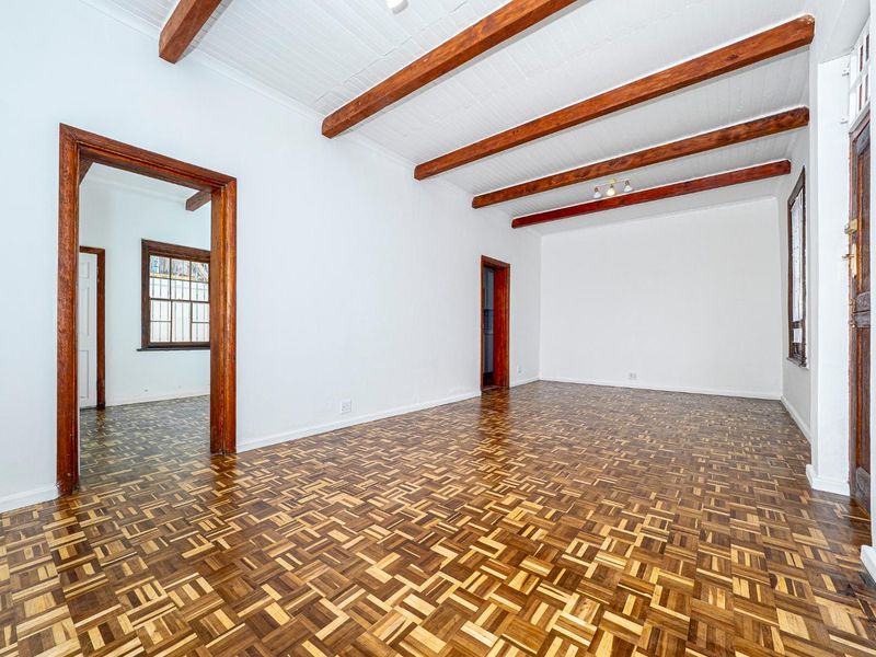 Spacious living area featuring classic parquet flooring, exposed timber ceiling beams, and traditional timber door and window frames.