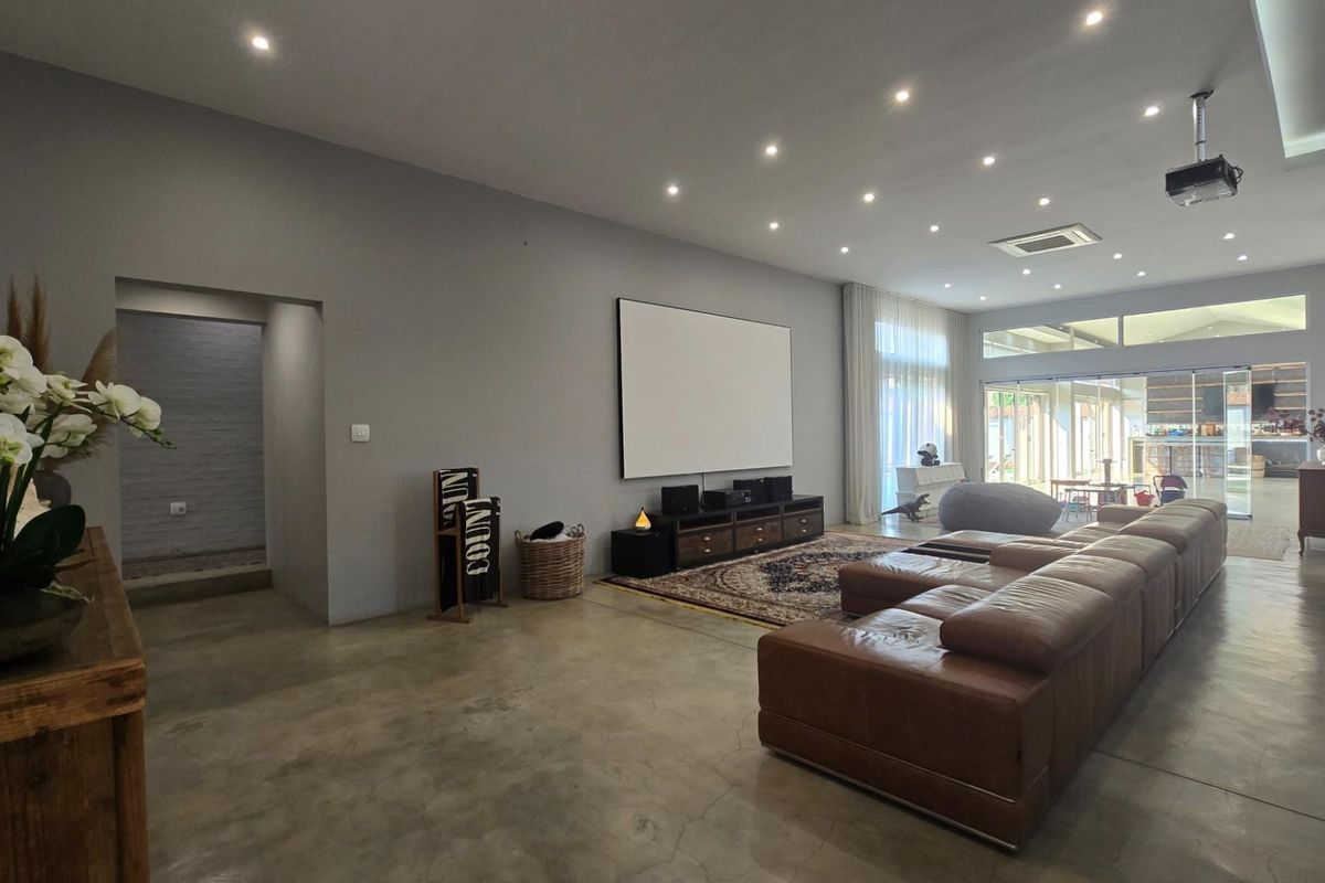 Spacious living area featuring polished concrete floors, recessed lighting, and a dedicated home cinema setup with a projection screen and ceiling-mounted projector.