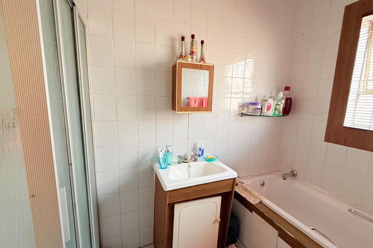 A compact bathroom featuring a built-in vanity, a bathtub with shower enclosure, and full-height wall tiling.