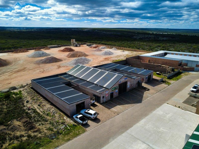 Aerial view of a commercial industrial property featuring multiple workshop units with metal roofing, paved parking areas, and a large rear storage yard.