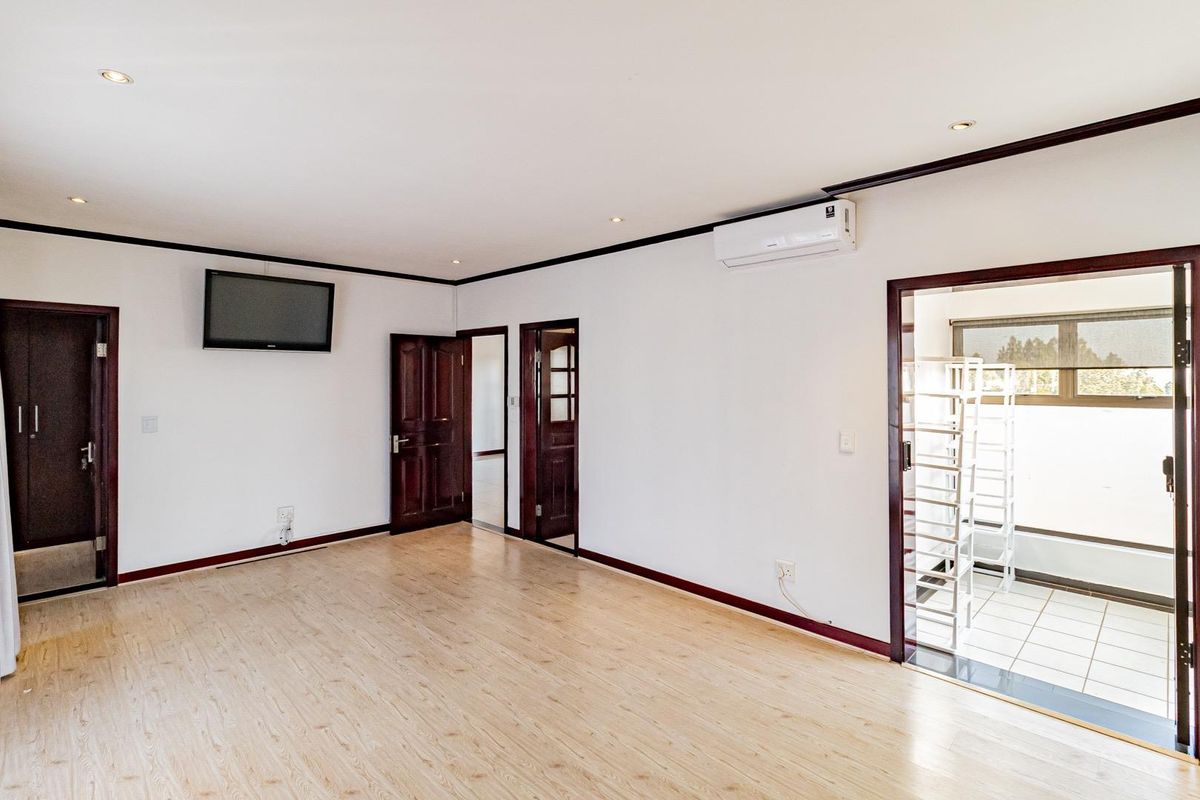 A spacious, empty room featuring light wood-look flooring, recessed ceiling lighting, a wall-mounted air conditioning unit, and dark wood door frames.