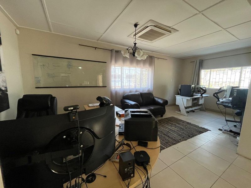A functional home office space featuring tiled flooring, a suspended ceiling with integrated air conditioning, and security bars on the windows.
