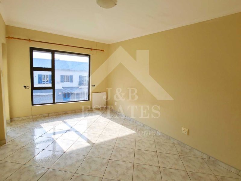 A bright, empty living room featuring neutral walls, tiled flooring, and a large window providing natural light.
