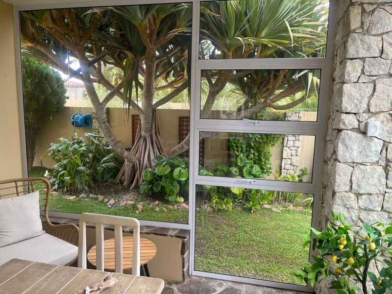 A bright, enclosed patio area featuring stone wall cladding, large aluminium-framed windows, and direct views of the landscaped garden.