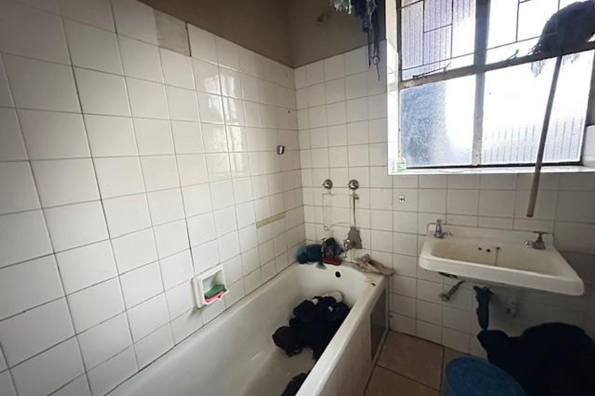 A dated bathroom featuring a standard bathtub, wall-mounted basin, and tiled walls, requiring significant renovation and modernization.