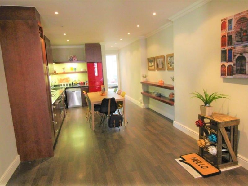 An open-plan living and kitchen area featuring modern dark wood cabinetry, integrated appliances, recessed lighting, and laminate flooring throughout.