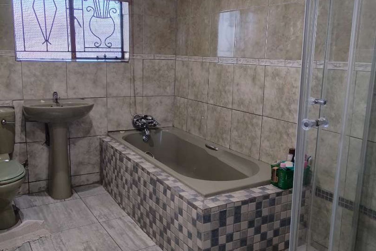 A functional bathroom featuring a built-in bathtub, separate glass-enclosed shower, pedestal basin, and tiled finishes throughout.