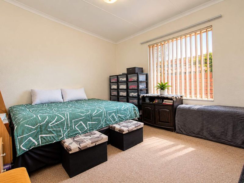 A functional bedroom featuring neutral wall finishes, carpeted flooring, and vertical window blinds, providing a comfortable and well-lit living space.
