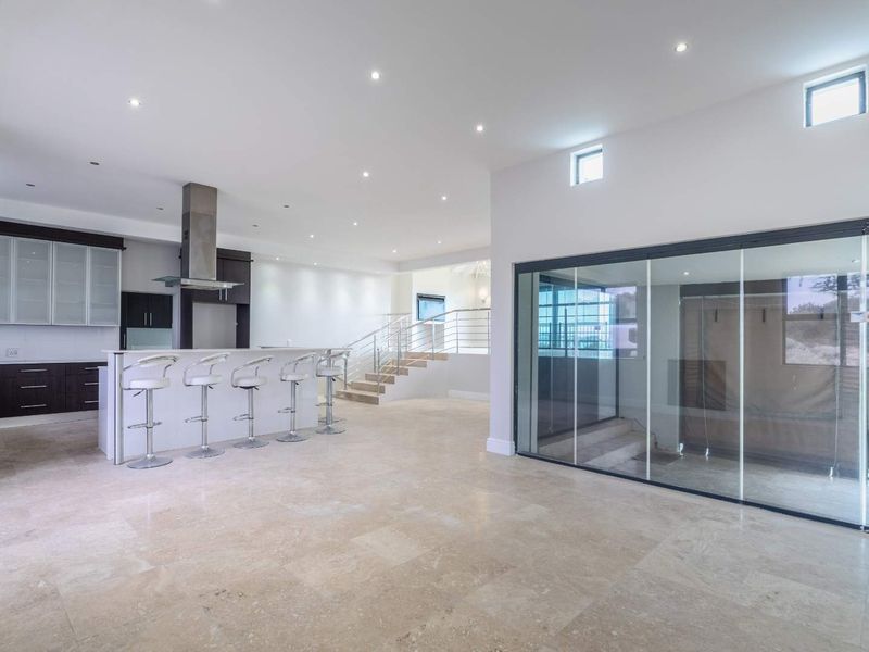 Spacious open-plan living area featuring a modern kitchen with island, stone flooring, and large sliding glass doors leading to the exterior.