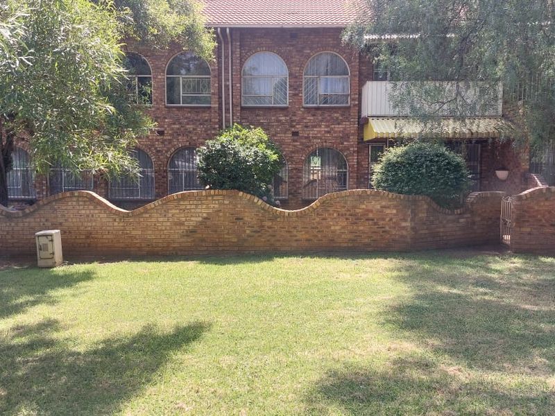 Rear view of a face brick apartment building featuring arched windows, security bars, and a private garden area with a curved brick boundary wall.
