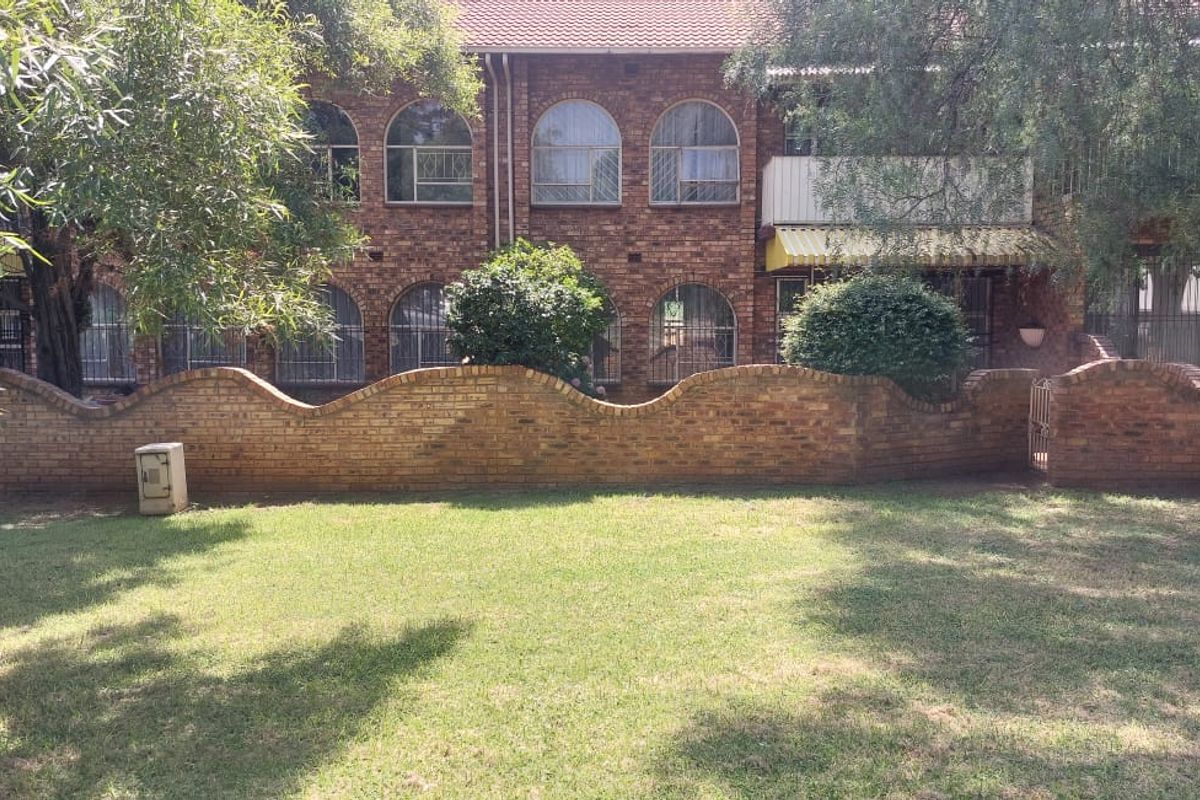 Rear view of a face brick apartment building featuring arched windows, security bars, and a private garden area with a curved brick boundary wall.