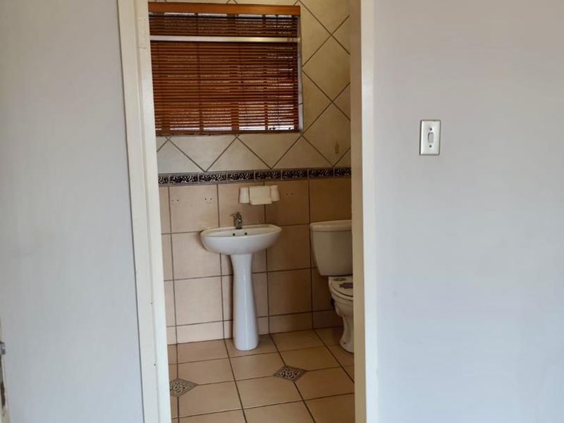 A functional bathroom featuring a pedestal basin, toilet, and neutral ceramic tiling throughout.