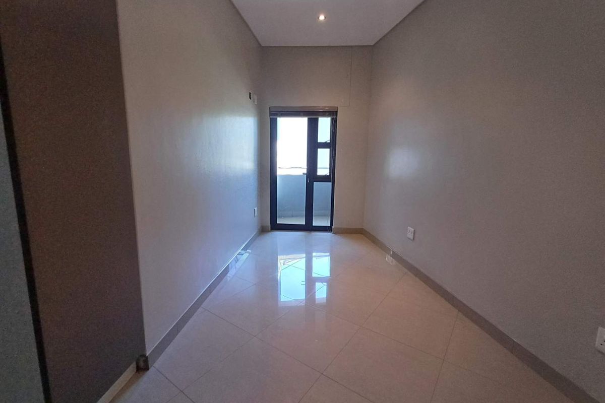 A bright, empty room featuring polished porcelain floor tiles, recessed ceiling lighting, and a glass-paneled door leading to an outdoor balcony.
