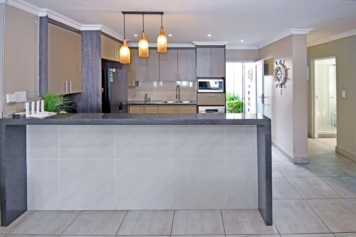 Modern kitchen featuring a granite breakfast bar, ample built-in cabinetry, integrated appliances, and tiled flooring, leading to an adjacent hallway.