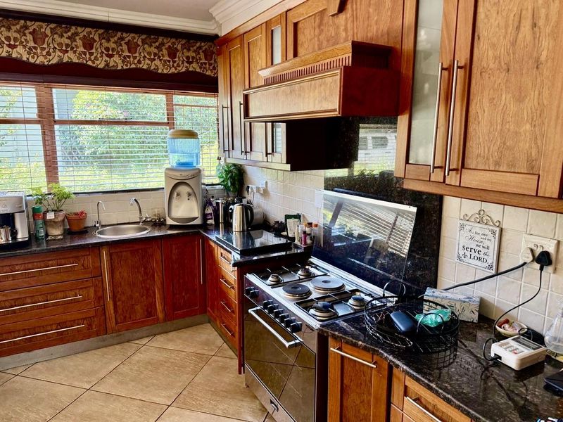 A functional kitchen featuring warm-toned wooden cabinetry, granite countertops, a built-in oven with hob, and a tiled backsplash with ample natural light.