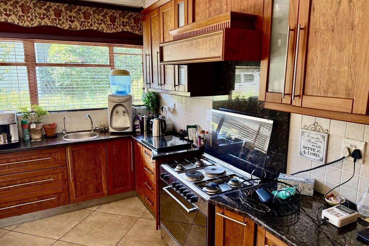 A functional kitchen featuring warm-toned wooden cabinetry, granite countertops, a built-in oven with hob, and a tiled backsplash with ample natural light.