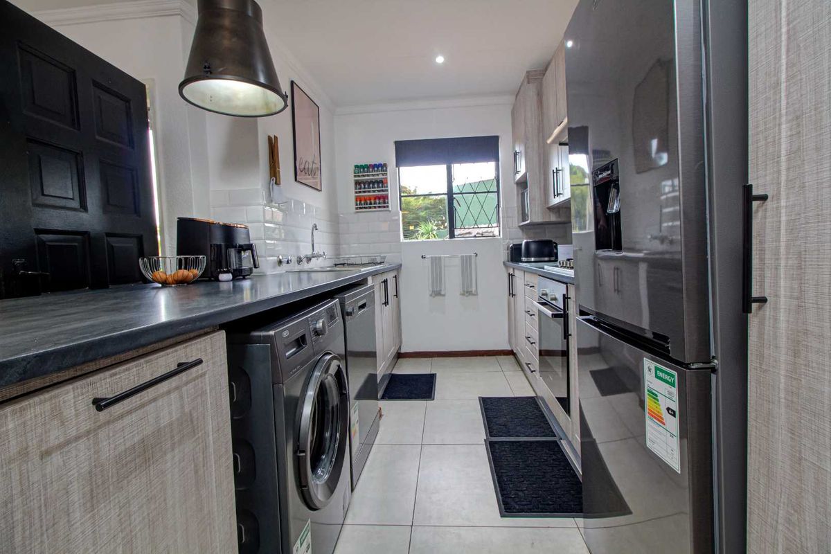 Modern galley-style kitchen featuring light wood-grain cabinetry, dark countertops, subway tile backsplash, and integrated laundry appliances.