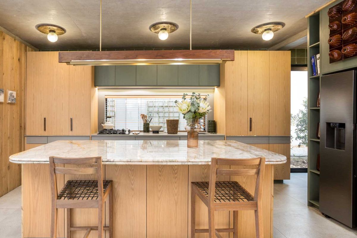 Modern kitchen featuring a large marble island, custom wood cabinetry, integrated appliances, and a raw concrete ceiling with stylish pendant lighting.