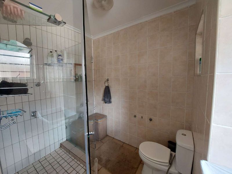 A functional bathroom featuring a glass-enclosed shower, ceramic wall and floor tiling, and a standard toilet suite.