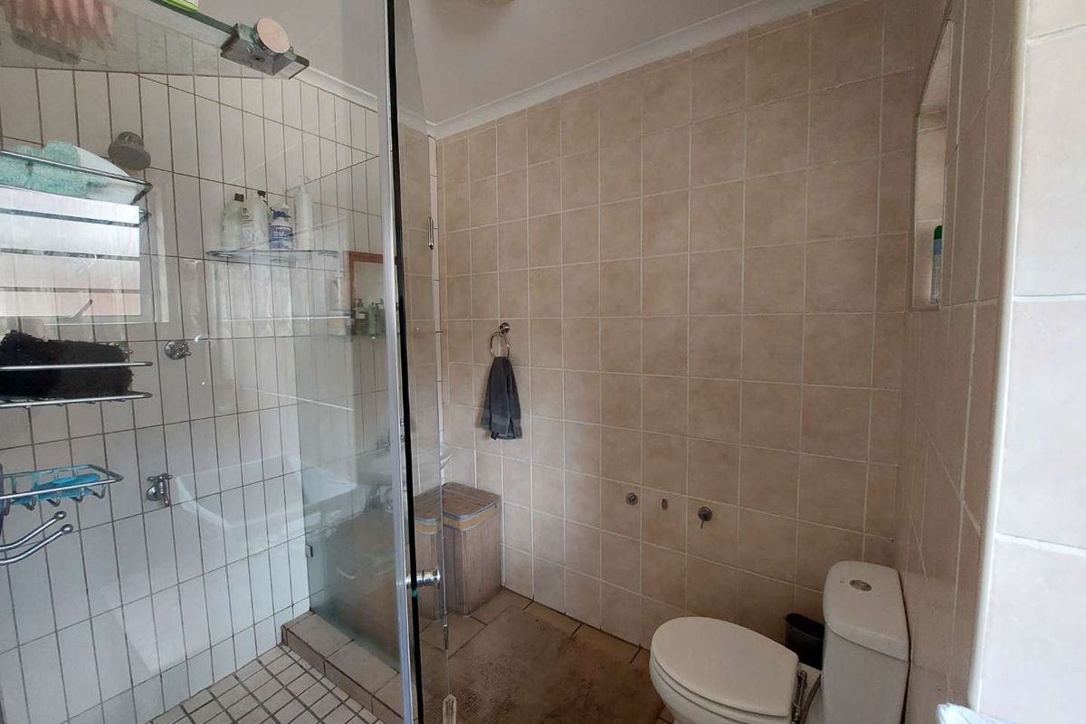 A functional bathroom featuring a glass-enclosed shower, ceramic wall and floor tiling, and a standard toilet suite.