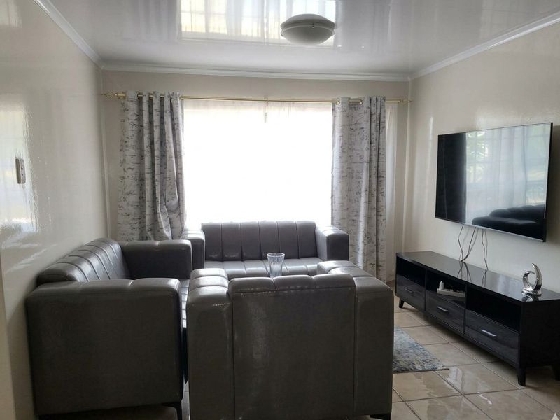 A well-maintained living room featuring tiled flooring, a coved ceiling, and a large window providing natural light.