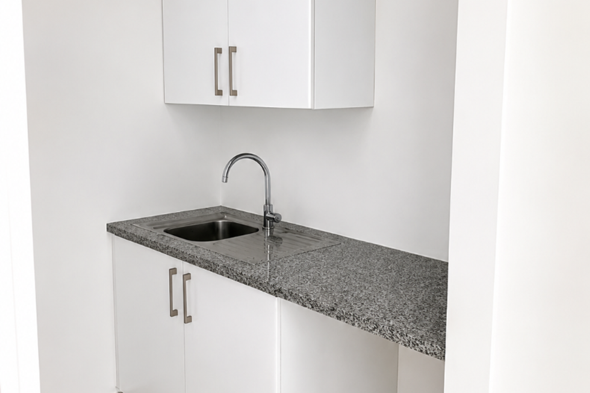 A clean, modern kitchenette featuring white built-in cabinetry, a granite countertop, and a stainless steel sink, suitable for office use.