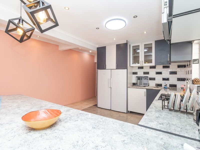 Modern kitchen featuring stone countertops, sleek two-tone cabinetry, a gas hob, and stylish subway tile backsplash with contemporary pendant lighting.