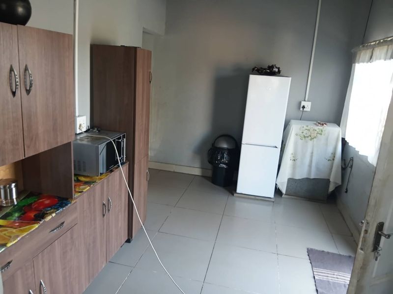 A functional kitchen area featuring wood-look cabinetry, tiled flooring, and surface-mounted electrical wiring.