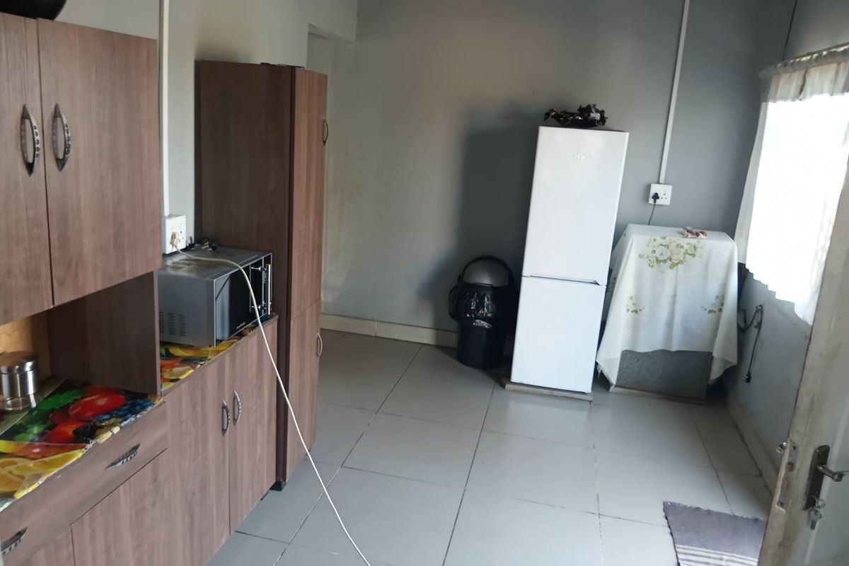 A functional kitchen area featuring wood-look cabinetry, tiled flooring, and surface-mounted electrical wiring.