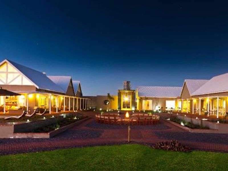 A beautifully illuminated farm estate at dusk, featuring multiple structures, a swimming pool, a central fire pit area, and extensive paved outdoor spaces.