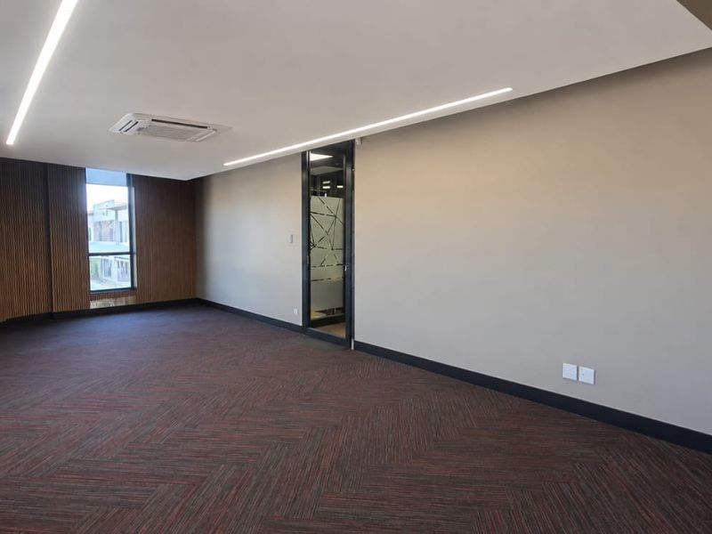 A modern, empty office space featuring timber wall paneling, recessed ceiling lighting, a cassette air conditioning unit, and herringbone carpet flooring.